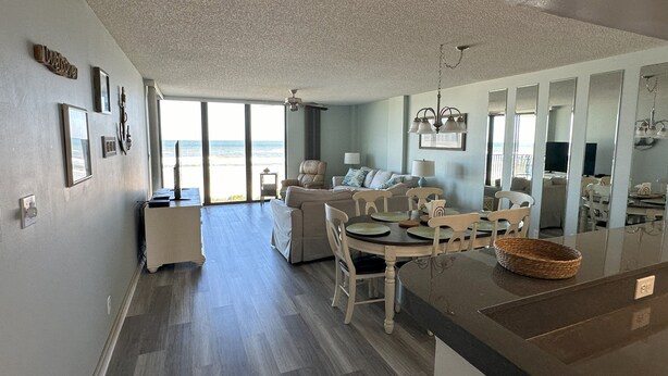 Ett rymligt vardagsrum med utsikt över stranden, en matplats med ett runt bord och ett kök med en stor köksö.