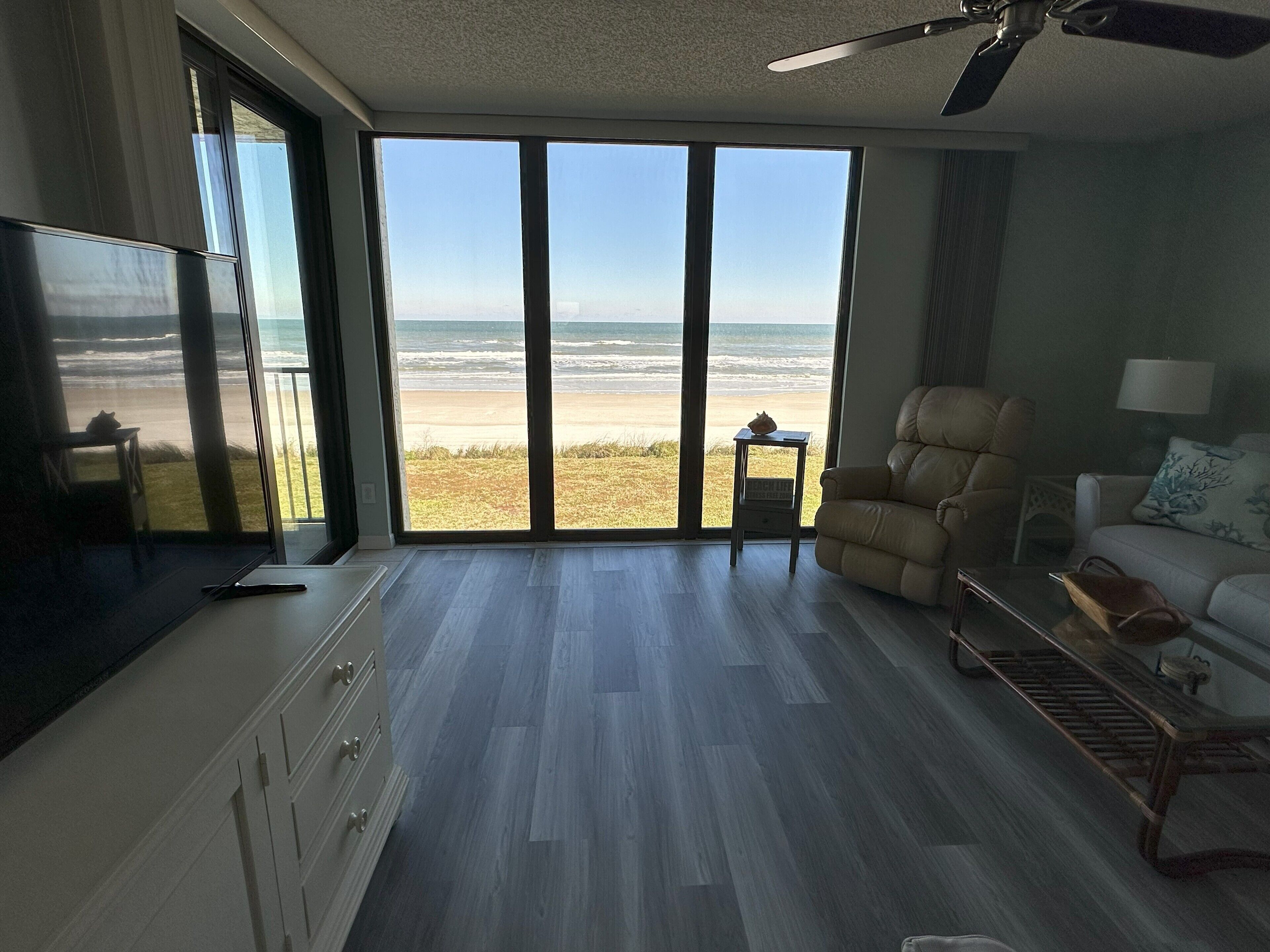 A spacious living room with a large sliding glass door leading to a beach view.