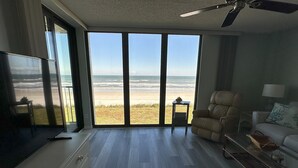 Ett rymligt vardagsrum med en stor skjutdörr i glas som leder ut till en terrass med utsikt över stranden.