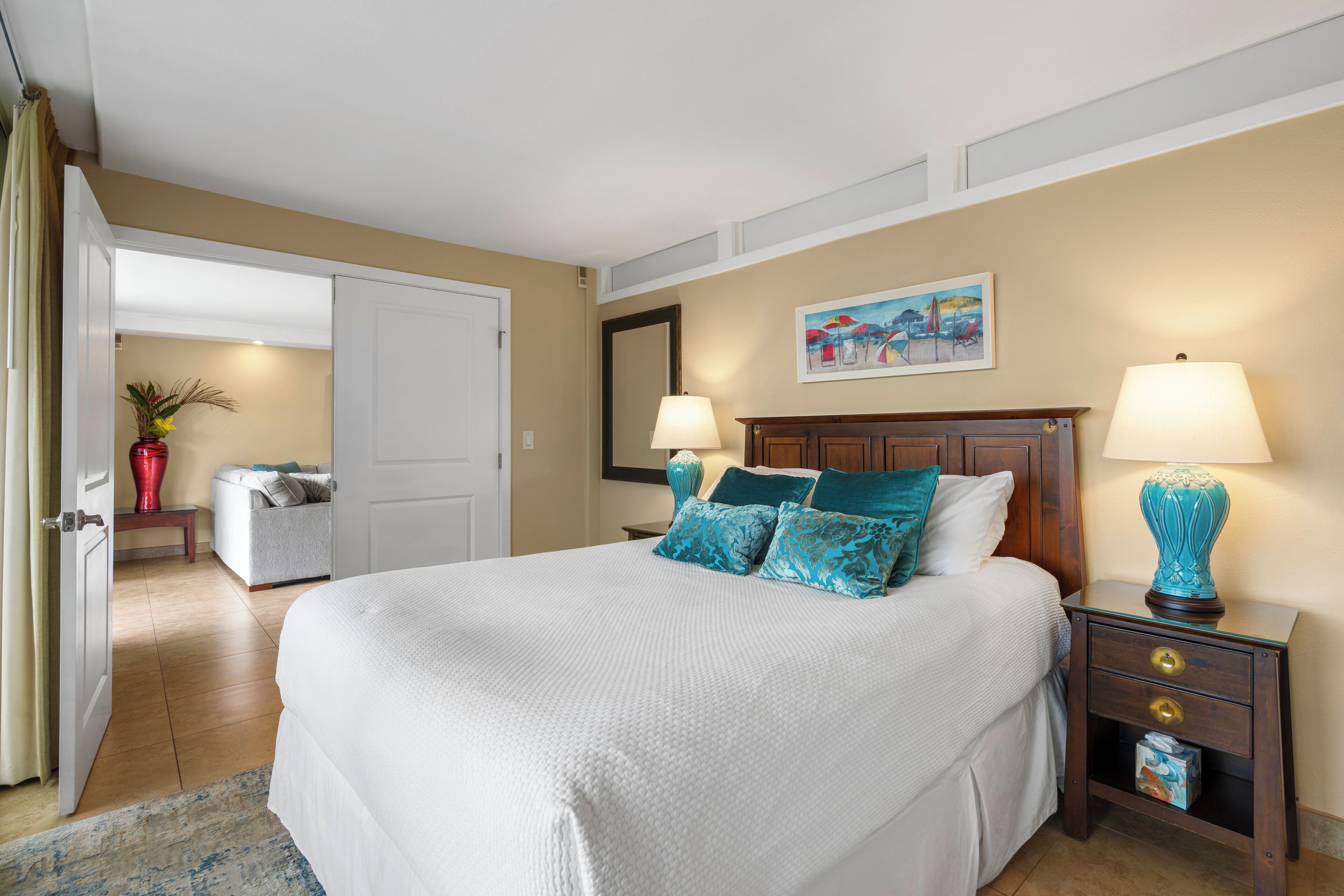 A neatly arranged bedroom with a large bed, bedside lamps, a nightstand, and a painting on the wall.