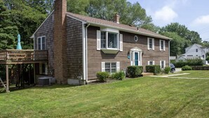 A two-story wooden house with a front porch, a visible chimney, and a small deck area. - Charming & spacious beach home in Bonnet Shores, Narragansett (Narragansett)