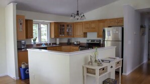 A kitchen with wooden cabinets, a central island, a refrigerator, and a microwave. - Charming & spacious beach home in Bonnet Shores, Narragansett (Narragansett)