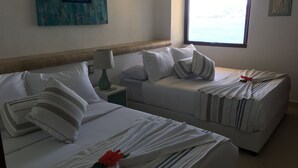 A hotel room with two beds, a nightstand with a lamp, a framed artwork on the wall, and a window with a view of the sea. - Los mejores atardeceres en Ixtapa Zihuatanejo (Ixtapa)