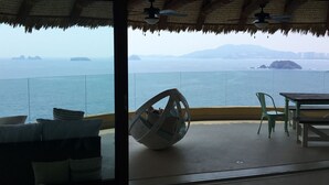 A balcony with a view of the sea, a ceiling fan, and a table with chairs. - Los mejores atardeceres en Ixtapa Zihuatanejo (Ixtapa)
