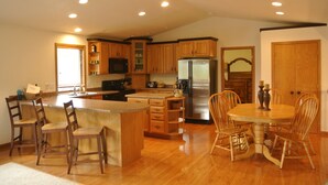 Una cocina amplia con armarios de madera, una isla central con taburetes de bar, un refrigerador de acero inoxidable y una mesa de comedor con sillas.