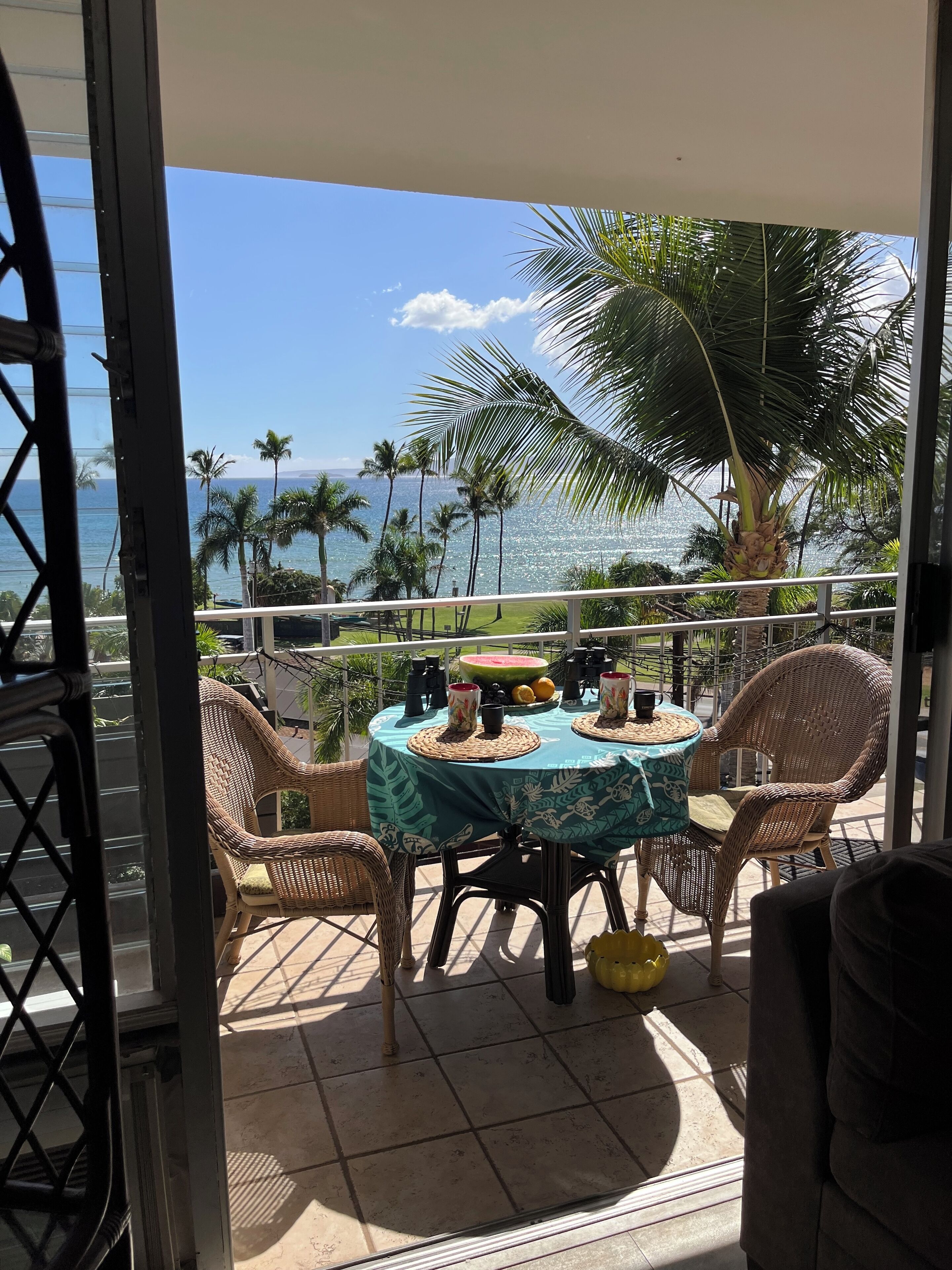 A balcony with wicker chairs, a table with a floral tablecloth, and a view of the ocean.