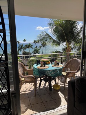 Ein Balkon mit Korbstühlen, einem Tisch mit blumigem Tischlein und Blick auf den Ozean.