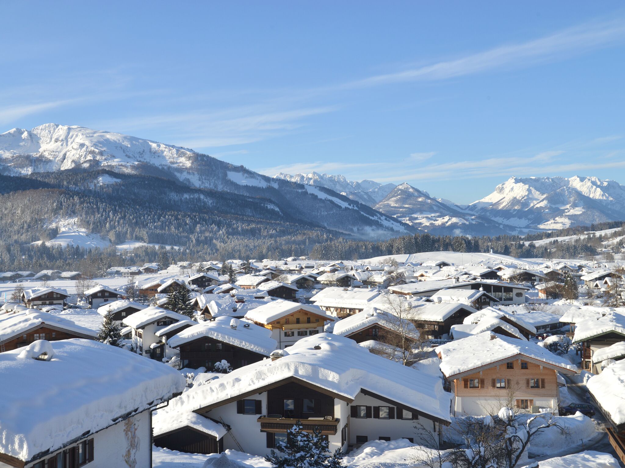 Un village enneigé, avec ses maisons traditionnelles en bois, un paysage montagneux en toile de fond et un ciel dégagé.