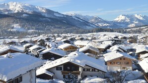 Un pueblo cubierto de nieve con casas de madera tradicionales, montañas al fondo y cielo despejado.