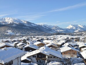 Un village enneigé, avec ses maisons traditionnelles en bois, un paysage montagneux en toile de fond et un ciel dégagé.