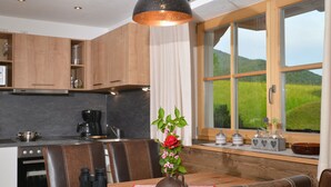 Una cocina moderna con armarios de madera, una mesa de comedor con sillas de cuero, una cafetera y vistas a un paisaje verde a través de amplios ventanales.
