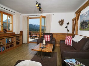 A cozy living room with a wooden floor, a brown leather sofa, a coffee table with a candle, and a bookshelf. - Ferienwohnung Talstation, 70 m² (Reit im Winkl)