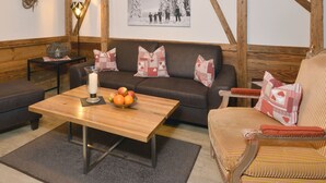 Un salón acogedor con pared de madera, un sofá marrón, una mesa de centro de madera con fruta y un cuadro enmarcado en la pared.