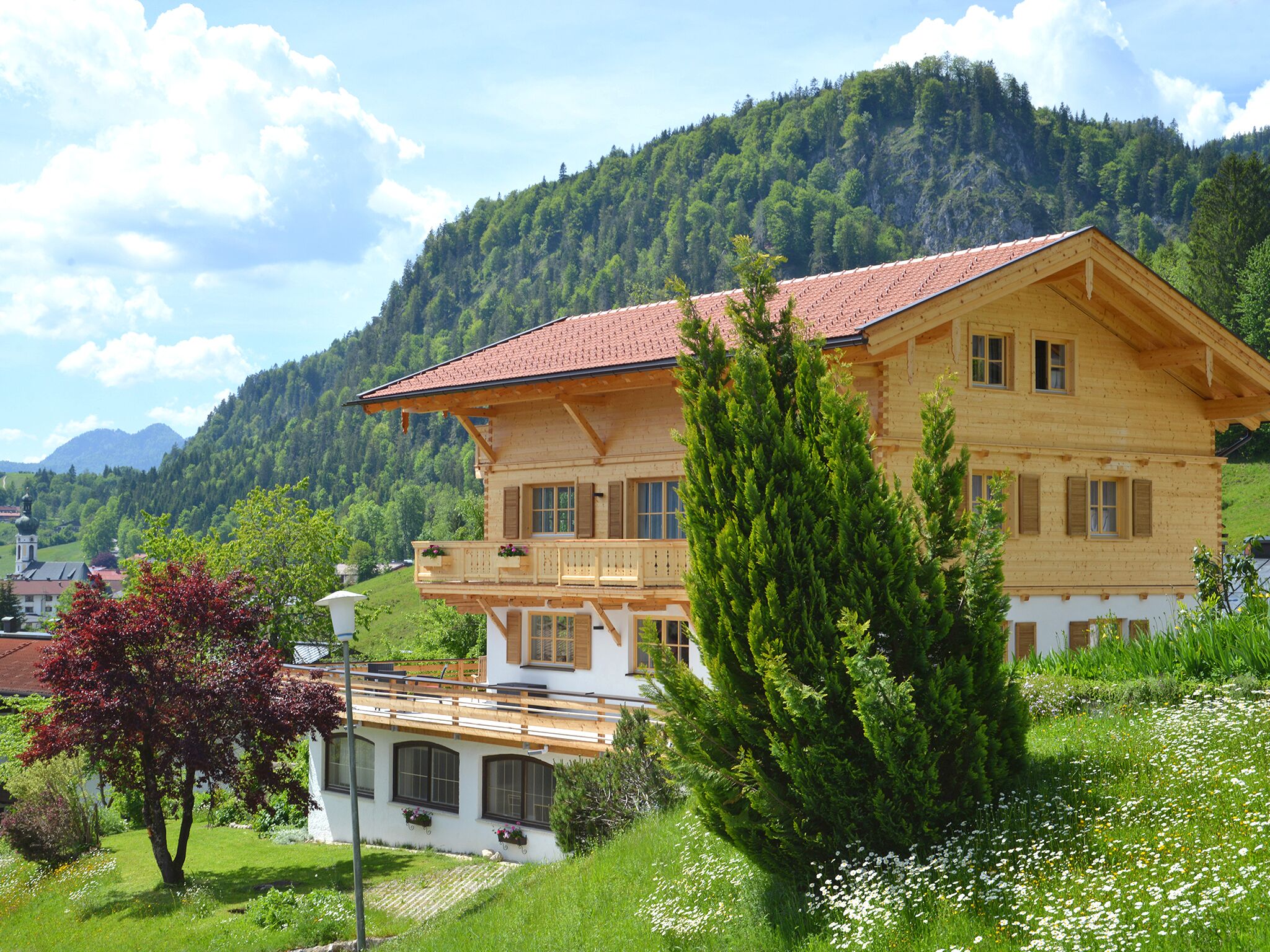 Un chalet en bois doté d’un balcon, entouré d’une végétation luxuriante et de montagnes.