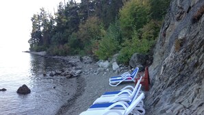 A rocky beach with lounge chairs lined up against a cliff. - Bella Cottage @ La Casa Lakeside Resort, 180 Degree View Of Lake Okanagan. (Kelowna)