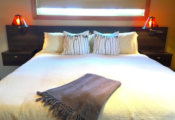 A neatly made bed with a white comforter and two pillows, flanked by nightstands with lamps. - Midwest Modern House (Austin)