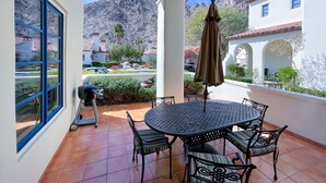 A covered patio with a round table and chairs, a grill, and a view of a mountainous landscape.