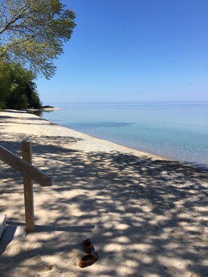 A beach with a wooden bench and a pair of shoes on the sand.