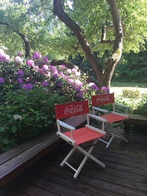 Relax on the deck with two comfortable chairs, surrounded by lush greenery and a majestic tree.