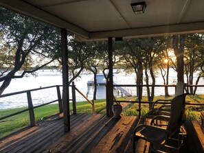 Um deck de madeira com guarda-corpo, vista para a água, uma cadeira e uma mesa.