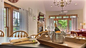 Un comedor con mesa de madera, sillas, una araña y vistas al exterior a través de amplios ventanales.