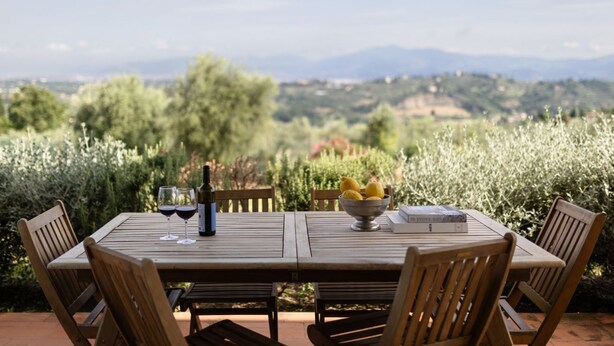 A wooden table with four chairs, a bowl of lemons, two wine glasses, and a bottle of wine. - Raffaello Apartment with garden (San Gersolé-torre Rosse)