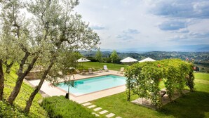 A swimming pool surrounded by lush greenery and a view of distant hills. - Raffaello Apartment with garden (San Gersolé-torre Rosse)