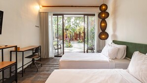 Een hotelkamer met twee bedden, een bureau en een stoel. Er is uitzicht op een tuin door een glazen deur.