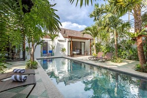 Un espace piscine avec des chaises longues, un coin salon abrité et un bâtiment doté d’un toit de chaume.