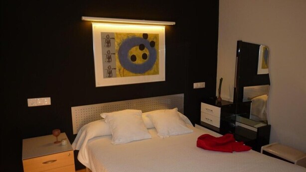 A hotel room with a bed, a nightstand, a dresser, and a wall-mounted artwork. - Leon apartments with two rooms (León)