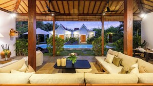 Een overdekt terras met een zwembad en een huis op de achtergrond.