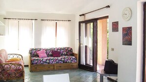 A cozy room with a floral sofa, a wicker chair, a small table, and a sliding glass door leading to an outdoor area. - JULY OFFER Sea View Granite House (Costa Paradiso)