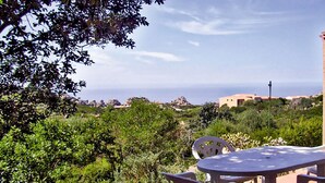 A patio with a table and chairs overlooking a coastal landscape with buildings and vegetation. - JULY OFFER Sea View Granite House (Costa Paradiso)
