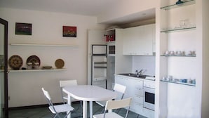 A compact kitchen with white cabinets, a built-in oven, and a refrigerator. There is a dining table with four chairs. - JULY OFFER Sea View Granite House (Costa Paradiso)