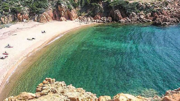 A coastal beach with clear turquoise waters and rocky cliffs. - JULY OFFER Sea View Granite House (Costa Paradiso)