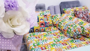 A bedroom with a bed covered in colorful bedding featuring animal prints, a grey headboard, and a grey rug.