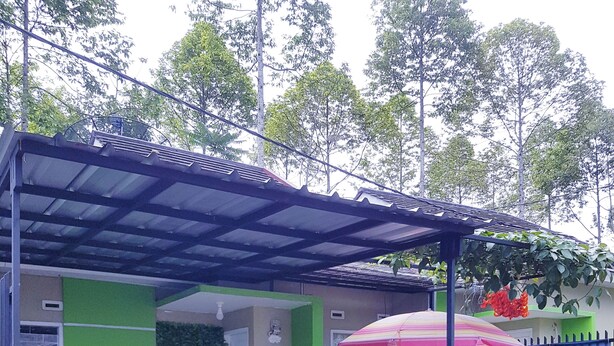 A covered outdoor area with a grill, a white picket fence, and a green wall.