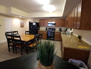 A kitchen with wooden cabinets, a dining table with chairs, a refrigerator, a microwave, and a stove. - MBV 4Br - Ocean Breeze (Myrtle Beach)