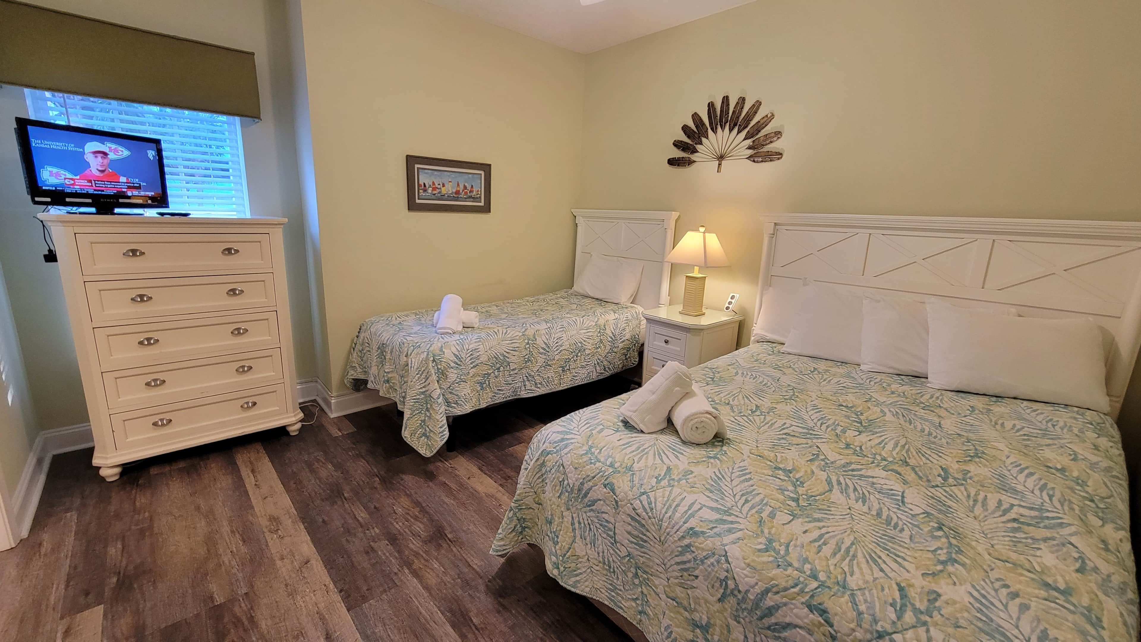 A hotel room with two beds, a dresser, a television, and a decorative wall piece.