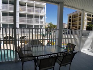 Un espacio al aire libre cubierto con piscina, una mesa con sillas y vistas a un edificio de varios pisos con balcones.
