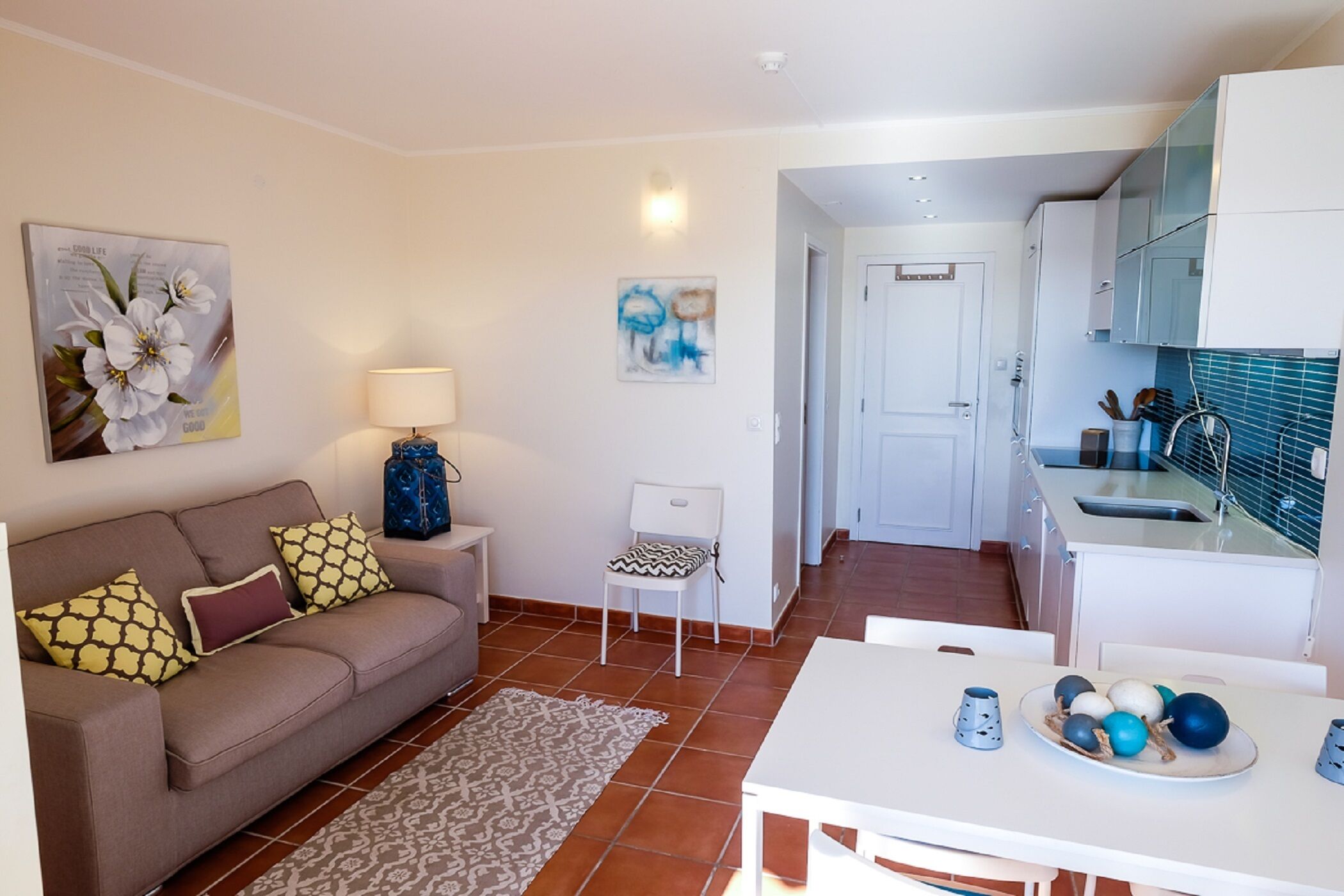 Un espace de vie compact comprenant un canapé, une petite table, une chaise et un coin cuisine avec des placards et un évier.
