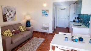 A compact living space with a sofa, a small table, a chair, and a kitchen area with cabinets and a sink. -   Modern 1 bedroom apartment on the sea front of Cabanas De Tavira   (Cabanas de Tavira)