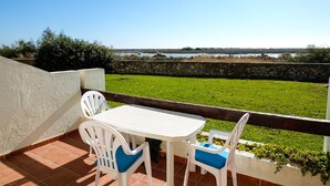 A patio with a white table and chairs, a stone wall, and a view of a grassy area and water body. -   Modern 1 bedroom apartment on the sea front of Cabanas De Tavira   (Cabanas de Tavira)