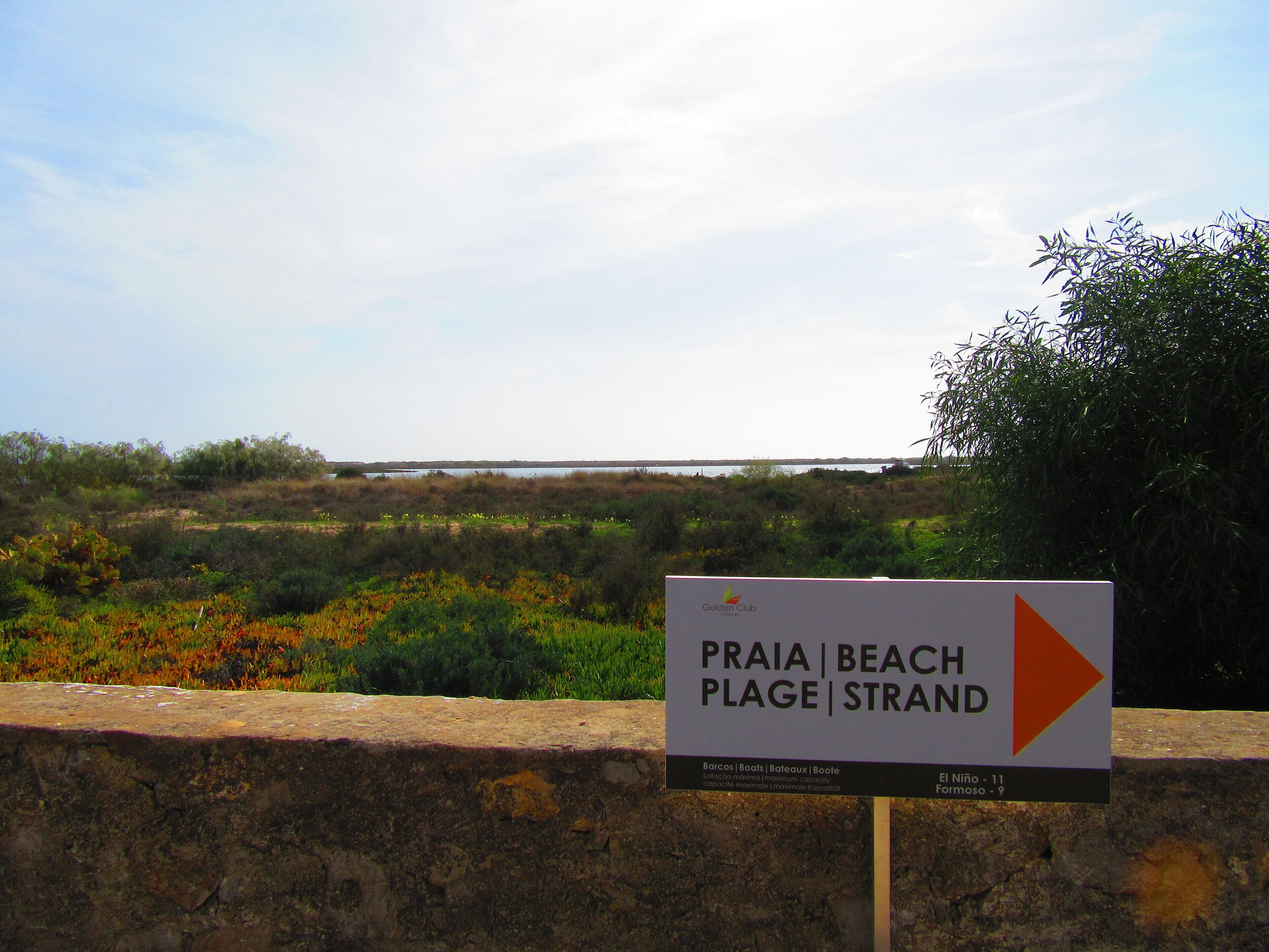 Un panneau indiquant la direction de la plage de Praia, avec une vue sur un paysage côtier.