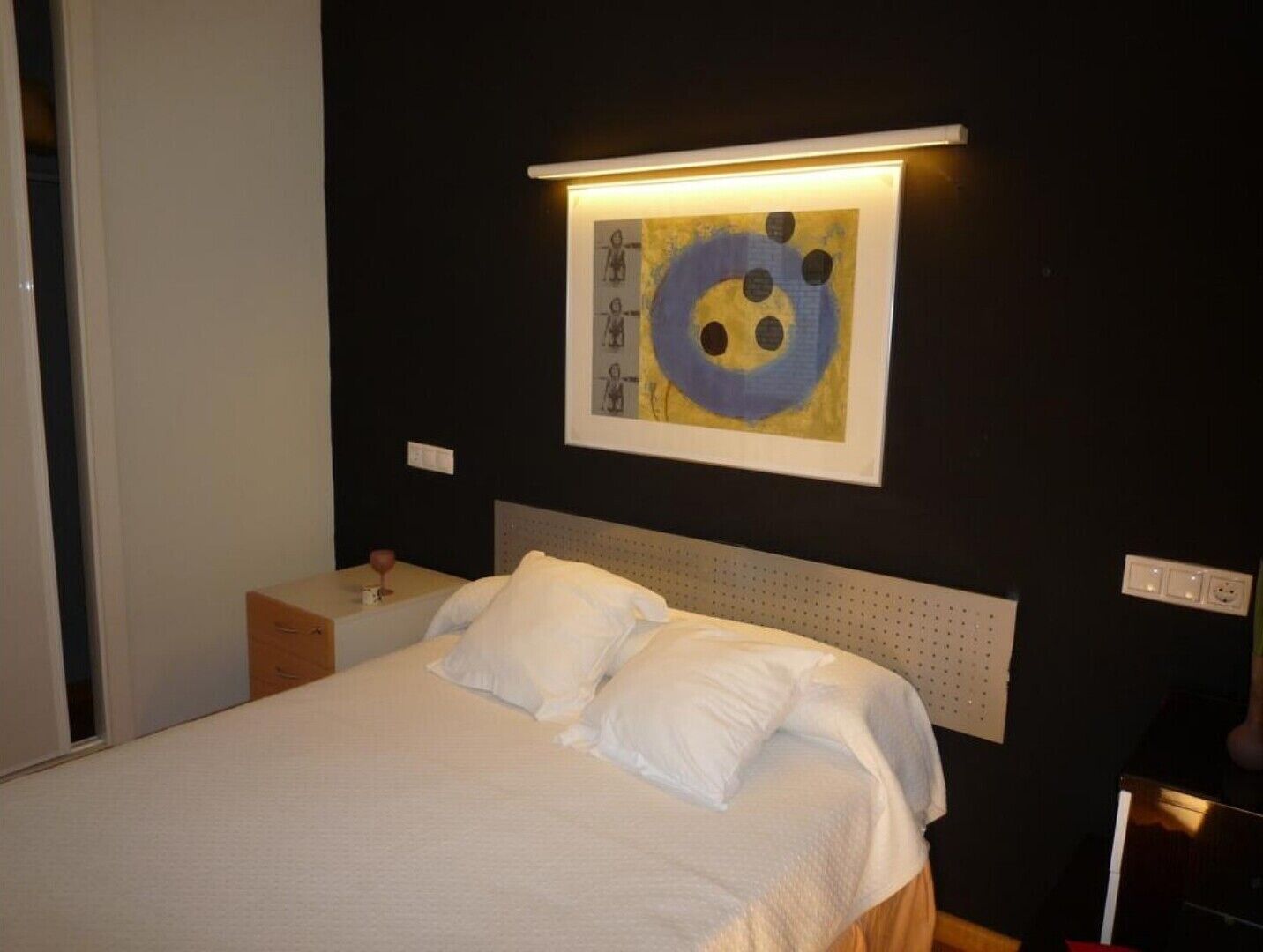 A hotel room with a bed, a nightstand, and a wall-mounted artwork.