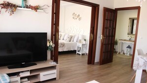 Een woonkamer met een televisie, een houten tv-meubel en een eethoek met een tafel en stoelen.