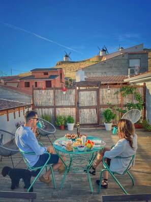A patio with a round table set for two, surrounded by chairs, with a view of windmills and buildings in the background. - Apartment 3 rooms ONCEMOLINOS (Consuegra)