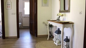 Een gang met een houten vloer, een witte muur met een inlijsting en een kleine tafel met een bloevas.