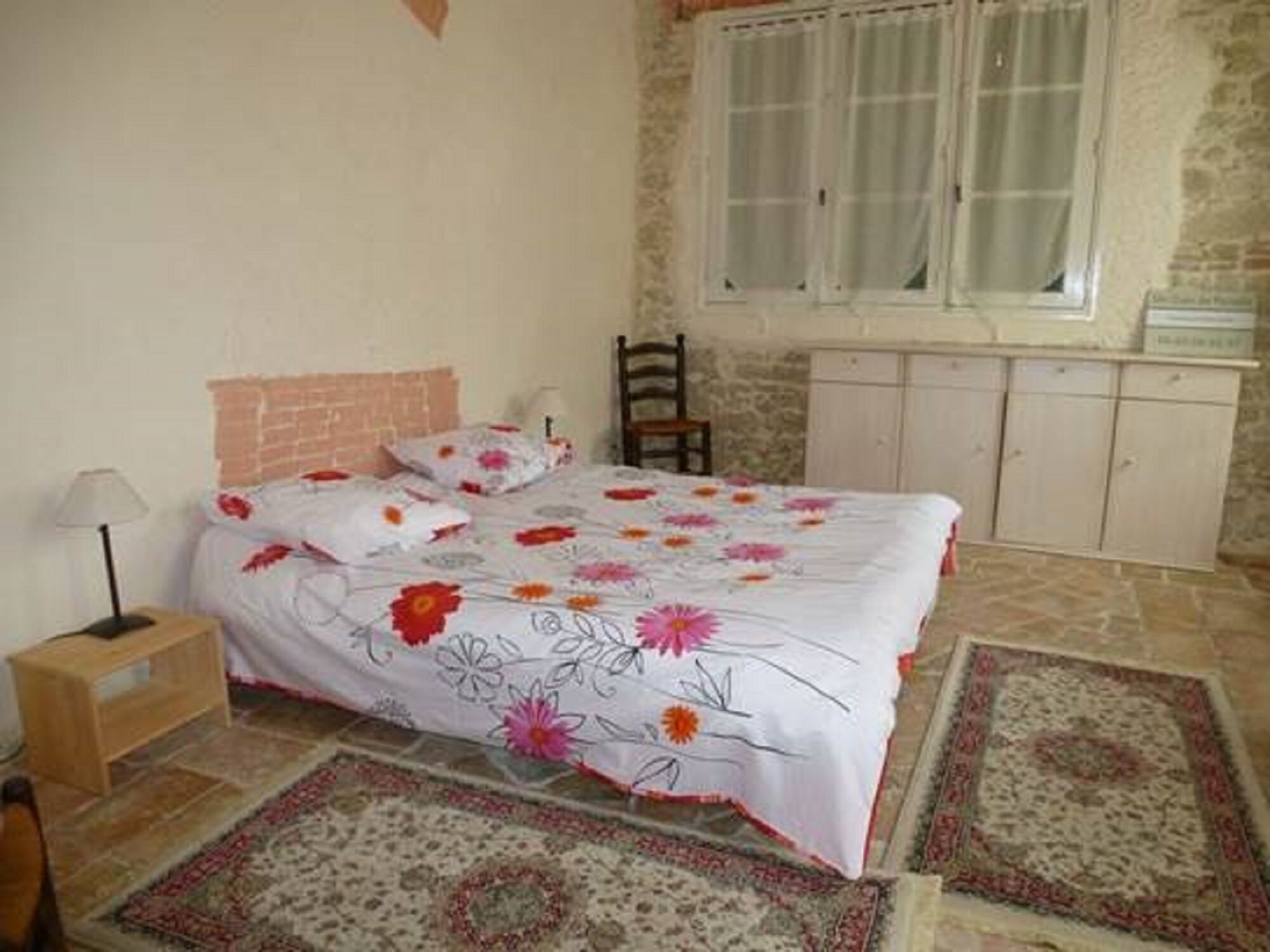 A bedroom with a bed, a nightstand, a chair, a wardrobe, and a window.