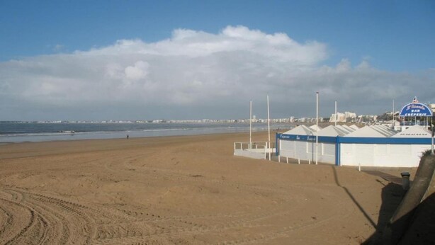 Una playa con una hilera de cabañas de playa y cielo despejado.